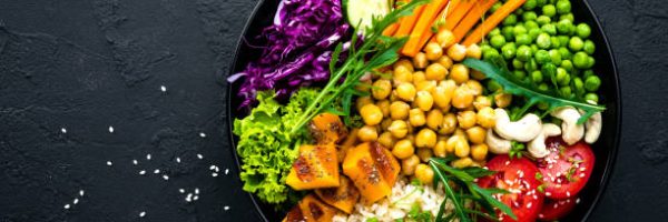 Bowl dish with brown rice, cucumber, tomato, green peas, red cabbage, chickpea, fresh lettuce salad and cashew nuts. Healthy balanced eating