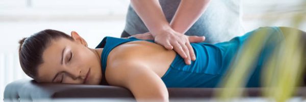 Massage therapist giving back massage to young woman. Patient lying on massage table.