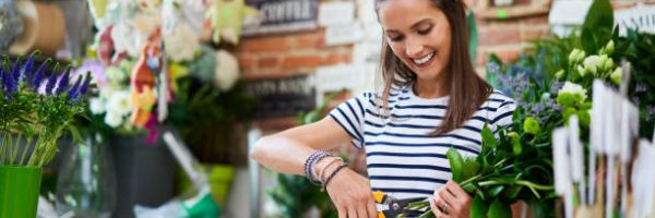 Cheerful young florist cutting flowers for bouquet at the counter