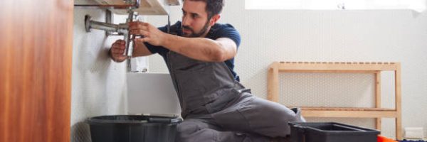 Male Plumber Working To Fix Leaking Sink In Home Bathroom