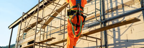 Construction worker wearing safety harness belt during working at high place at construction site.