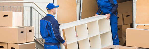 Young male movers unloading furniture and cardboard boxes from truck on street