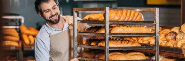 smiling male shop assistant arranging fresh pastry in supermarket