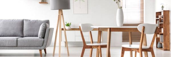 Wooden chairs at table in bright open space interior with lamp next to grey couch